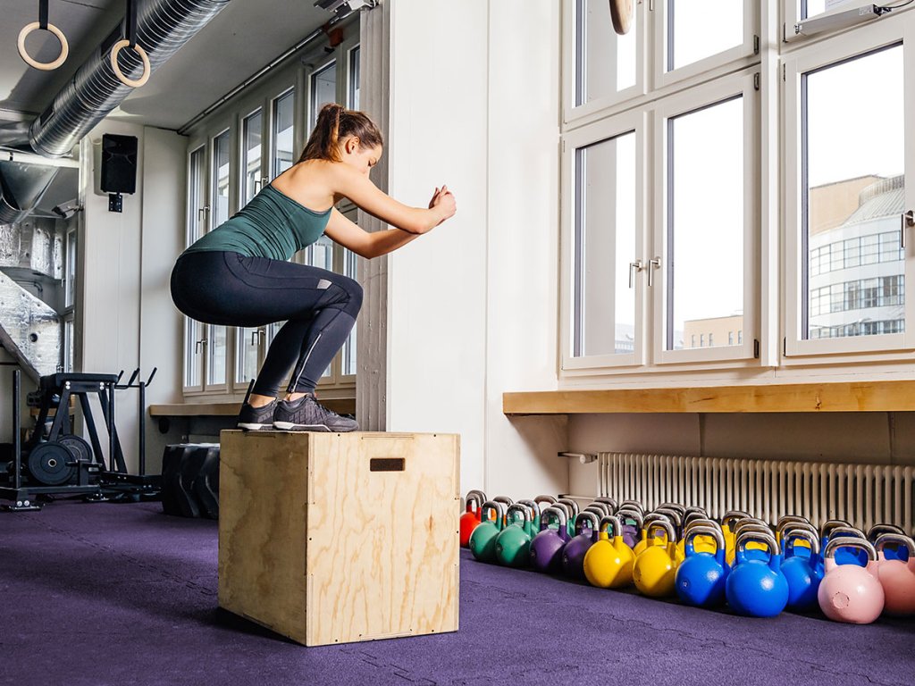 Woman performing a box jump in a gym setting.