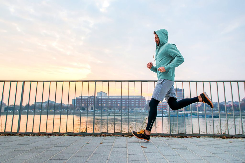 Man in a green hoodie running along a body of water.