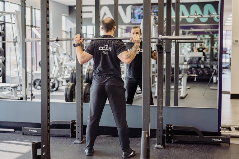 Coach Mike facing a squat rack, holding the barbell on his shoulders.