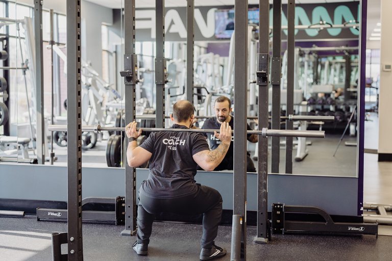 Coach Mike doing a full, deep squat with the barbell on his shoulders.