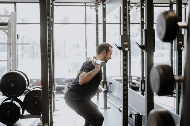 Coach Mike starting to squat with a barbell resting on his shoulders. His back is straight and angled forward, and his knees are bent.