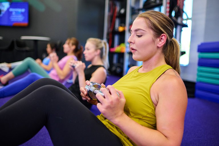 Woman doing a sit-up in the gym while holding a hand weight.