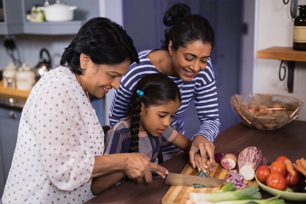 Grandmother, mother, and young daughter preparing healthy food in the kitchen.