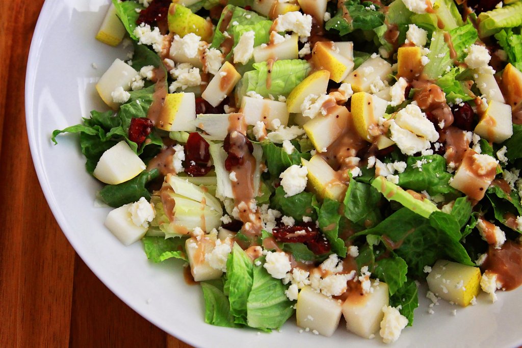 Bowl filled with lettuce, chopped pears, feta cheese and dressing mixed together.