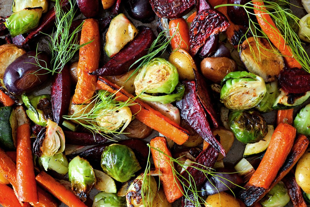 Top-down image of roasted vegetables mixed together on a baking sheet.
