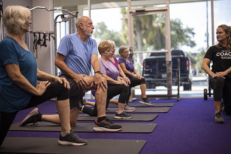 Joe performing a warm-up in a small-group training class at the gym with his Coach and other participants nearby.