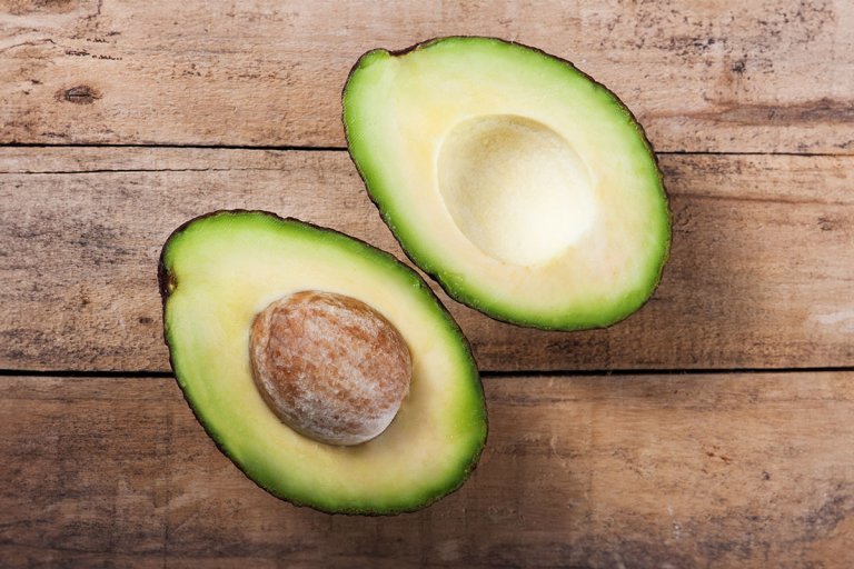 Two avocado halves sitting face up, side by side on a wooden surface.