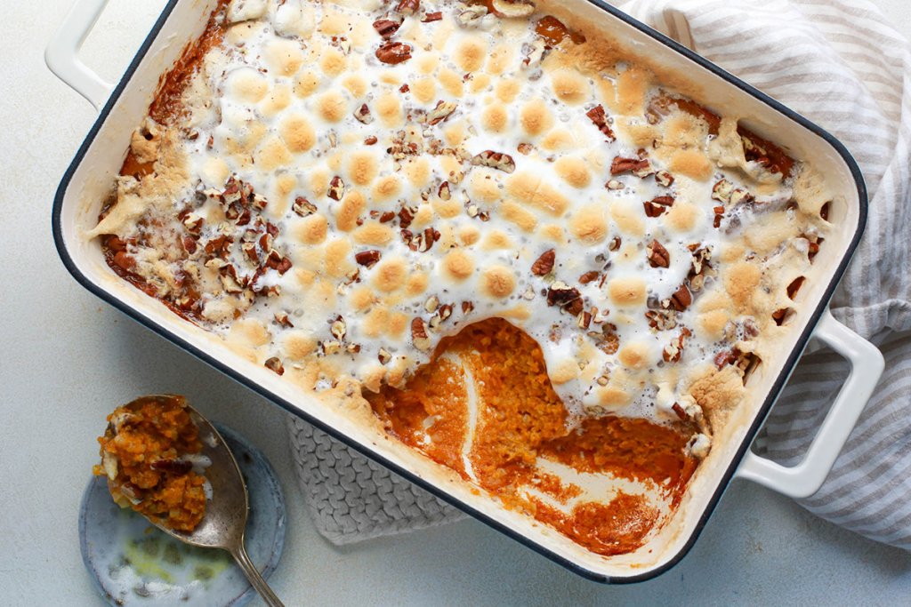 Sweet potato casserole in a baking dish, a scoop removed, with a serving spoon sitting next to the dish.