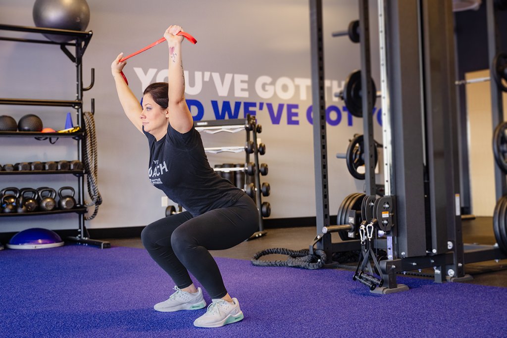 Woman performing a lunge in a gym setting while holding a red resistance band overhead.
