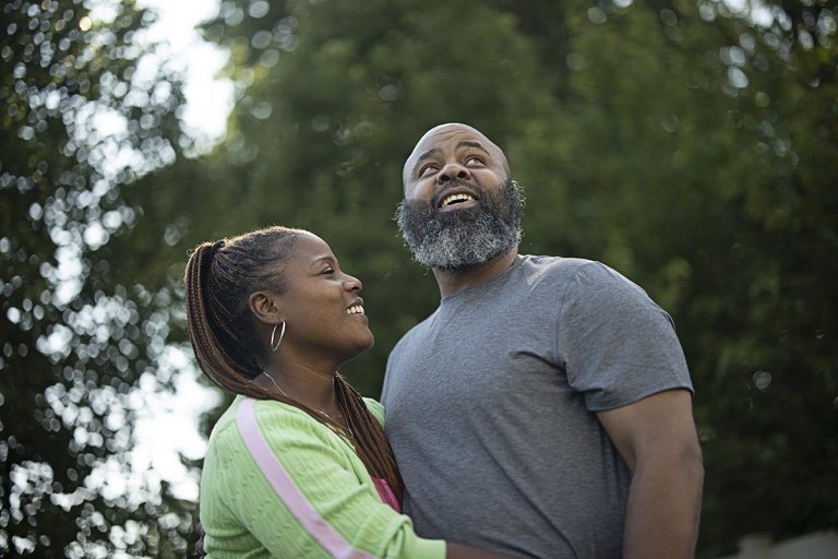Mark and his wife standing in a wooded area, smiling and hugging.