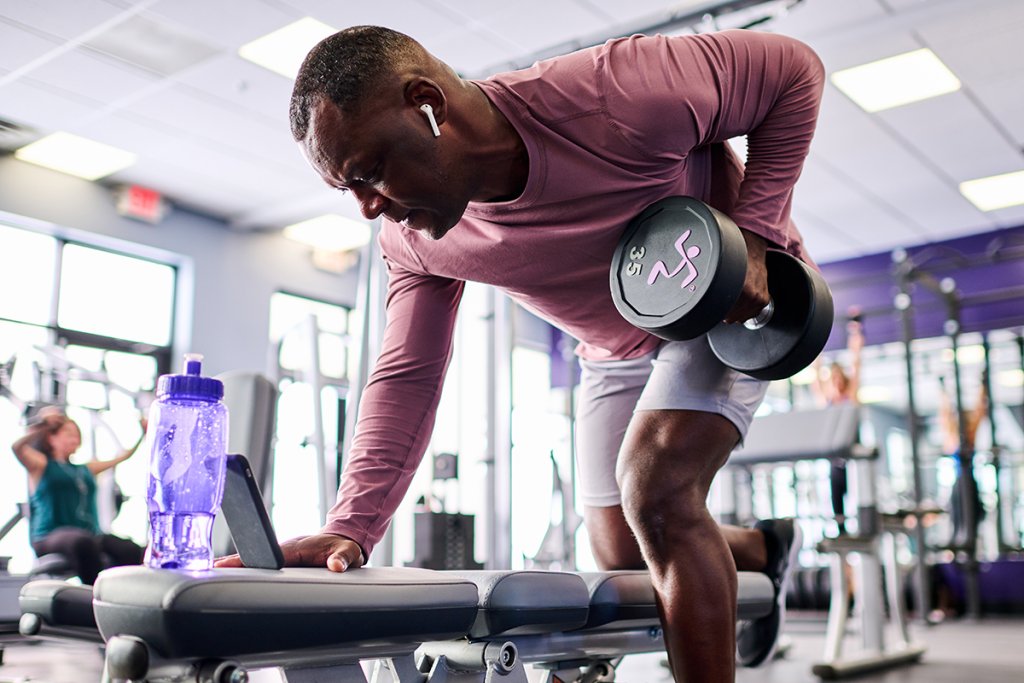 Man in a gym working his pulling muscles with a dumbbell.