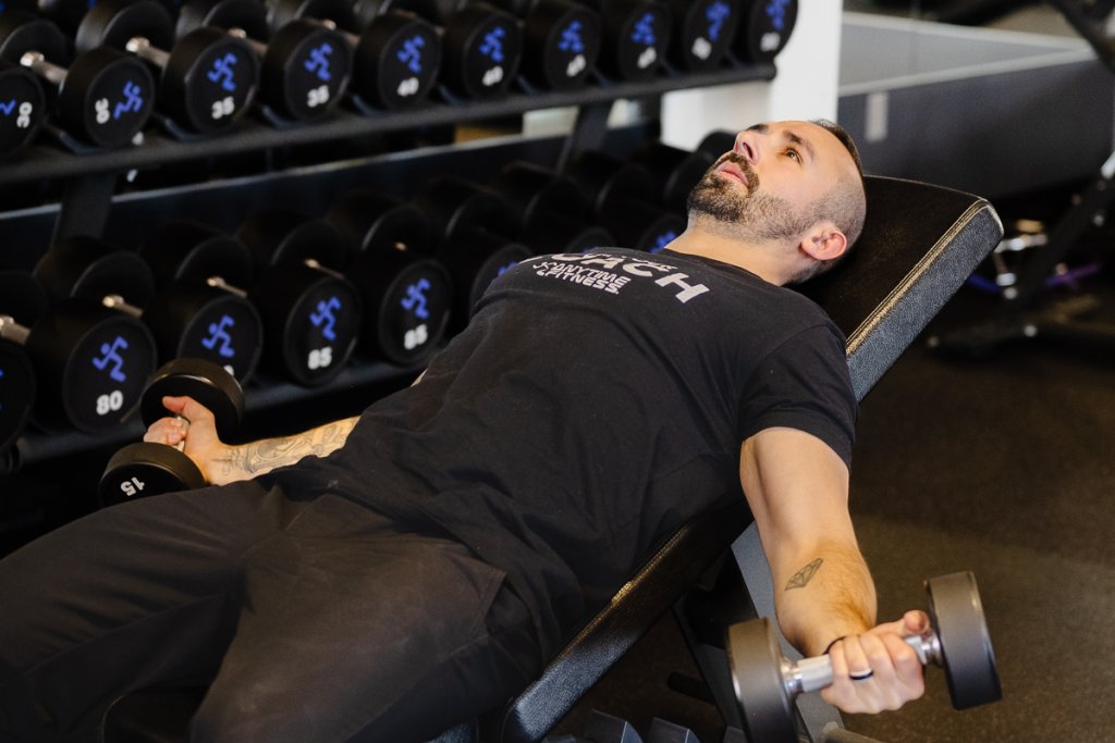 Man lying on a gym bench doing the incline dumbbell fly.