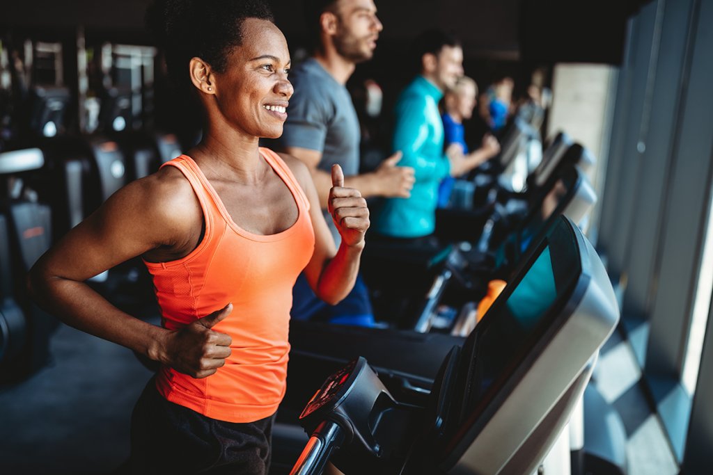 Woman in an orange shirt running on a treadmill in a gym.
