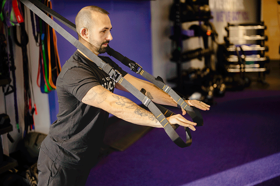 Anytime Fitness Coach Mike demonstrating a TRX push-up in a gym setting.