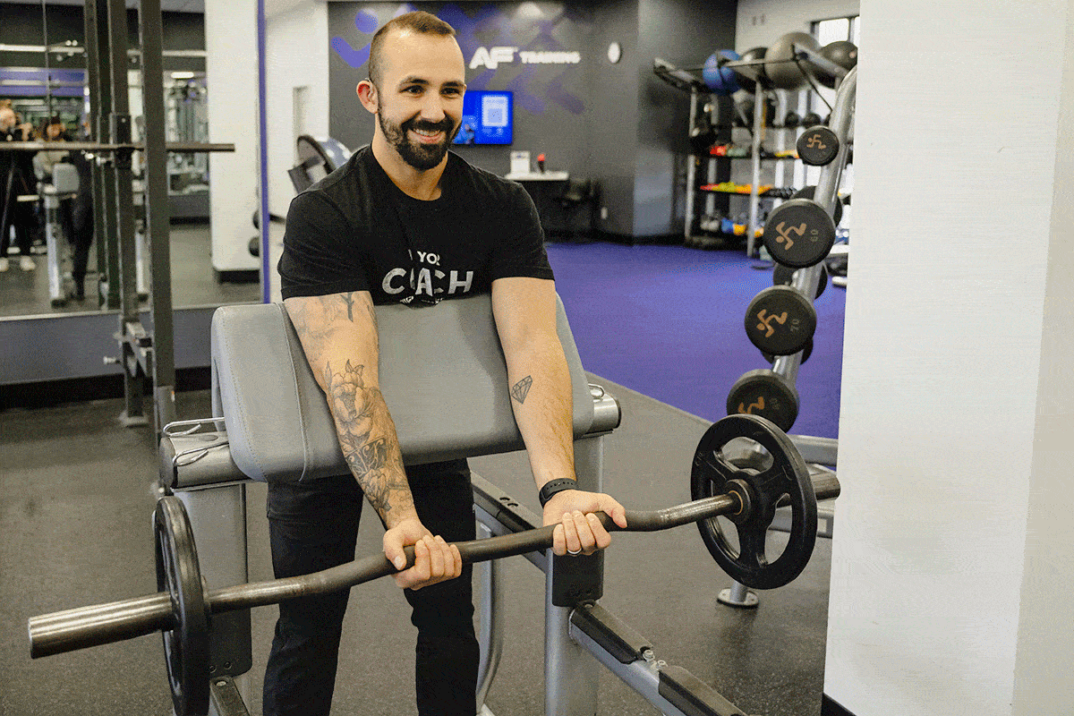 Coach Mike demonstrating preacher curls with a barbell in a gym setting.