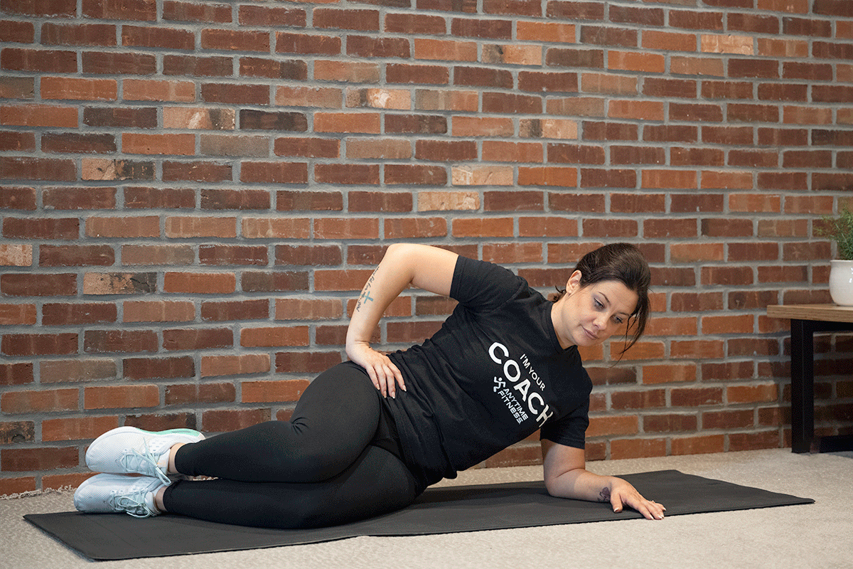Woman performing a side-plank clam on a yoga mat.