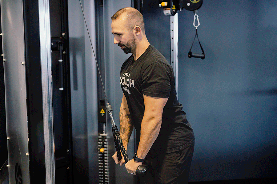 Man in a gym performing reps of a cable triceps pushdown.