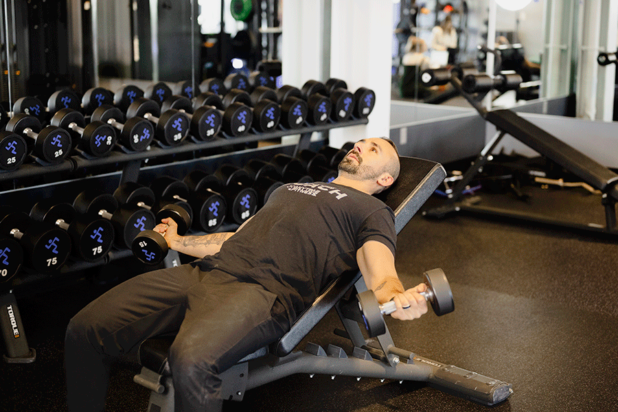 Man lying on an incline gym bench doing reps of an incline dumbbell fly.