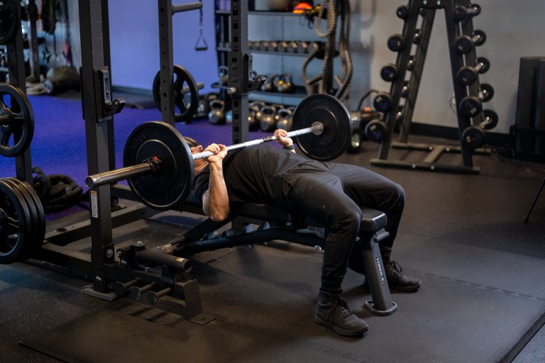 Anytime Fitness Coach Mike demonstrating how to bench press with proper form while lowering the barbell.