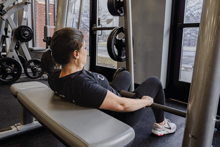 Coach Heather performing a hip thrust on a Smith machine while strength training in a fitness center.