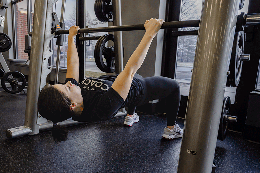 Coach Heather performing an inverted row on a Smith machine while strength training in a fitness center.