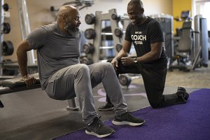 Coach Devon is near Mark as he does a tricep dip on a bench in a gym setting.