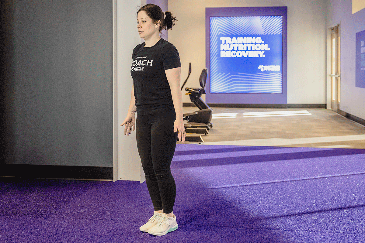 Woman in a gym hopping into a squat then lowering her hands to the floor between her legs