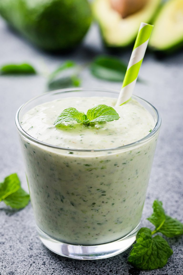 Close-up image of one green smoothie with a green straw, made with avocado, mint, spinach, banana, and chia seeds.