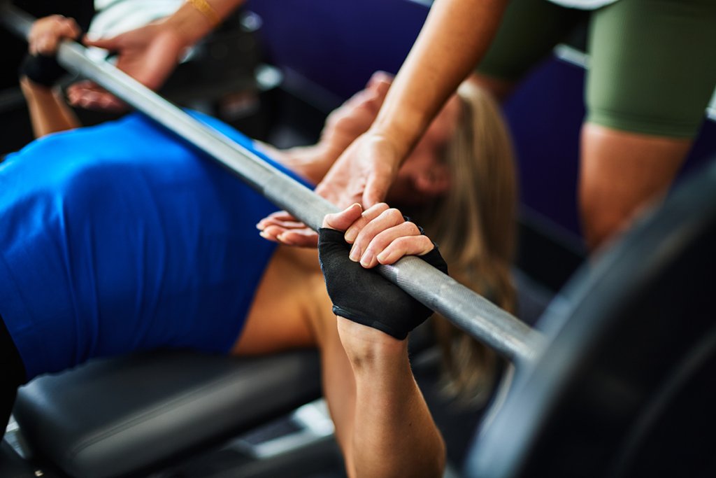 Woman performing a barbell bench press with a spotter.