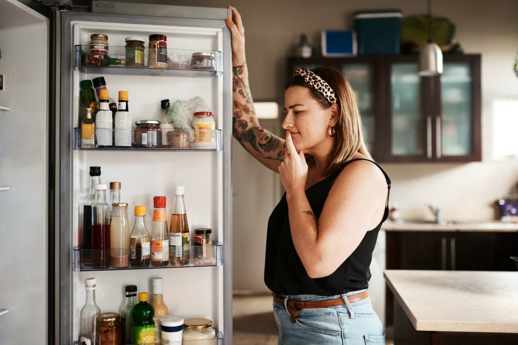 Shot of a young woman searching inside a refrigerator at home.