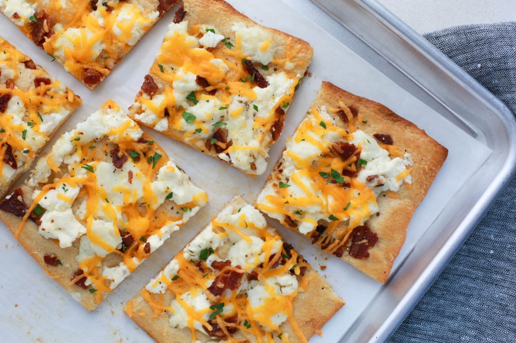 Square slices of breakfast pizza, made with eggs, cheese and bacon crumbles, on a pan lined with parchment paper