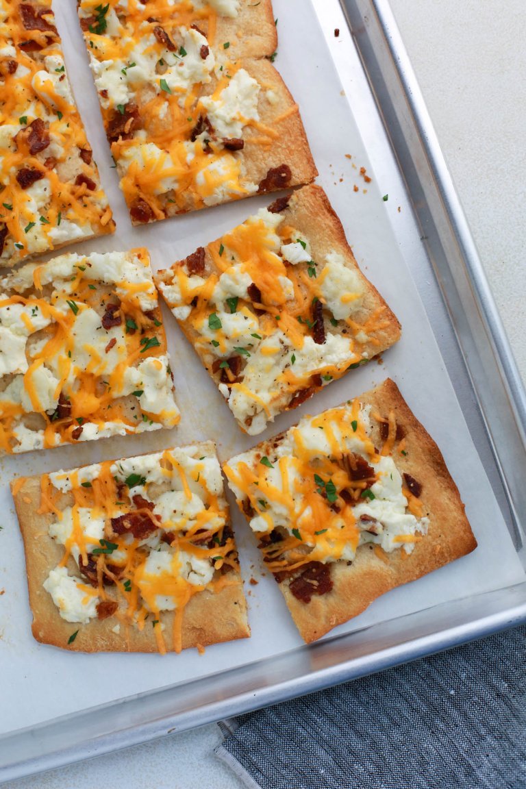 Square slices of breakfast pizza, made with eggs, cheese and bacon crumbles, on a pan lined with parchment paper