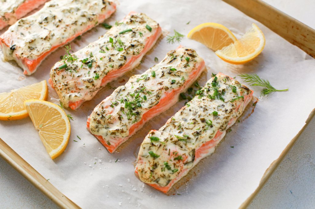 Salmon filets prepared on a pan lined with parchment paper with herb topping and lemon wedges
