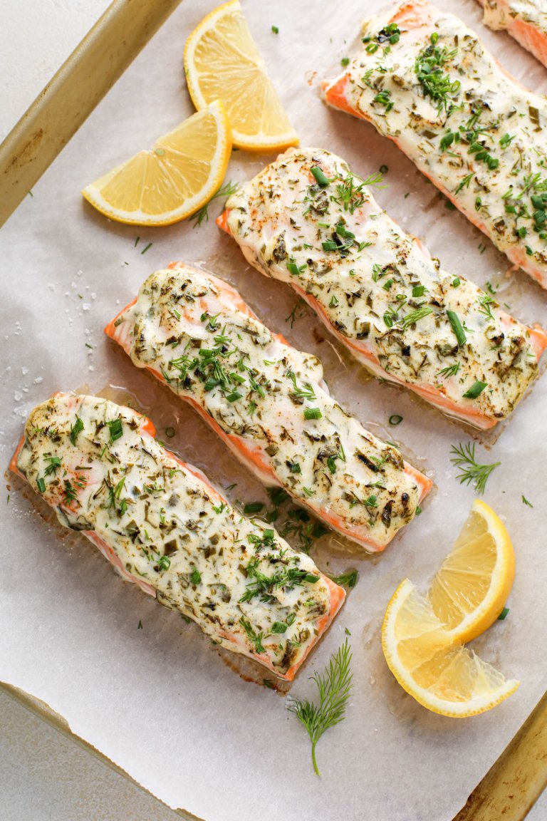 Salmon filets prepared on a pan lined with parchment paper with herb topping and lemon wedges