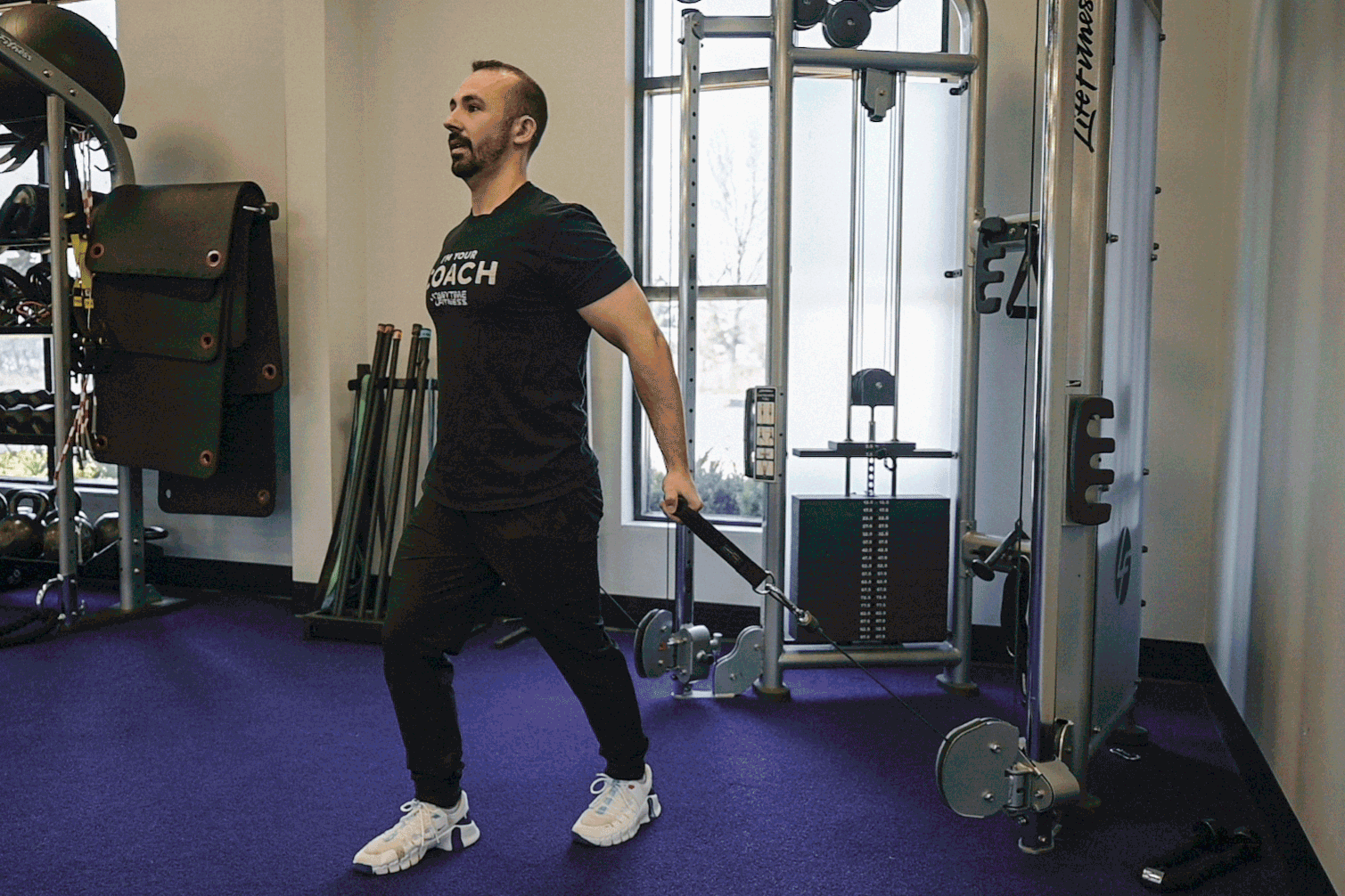 Coach Mike demonstrating a low pulley crossover on the cable machine in a gym setting.