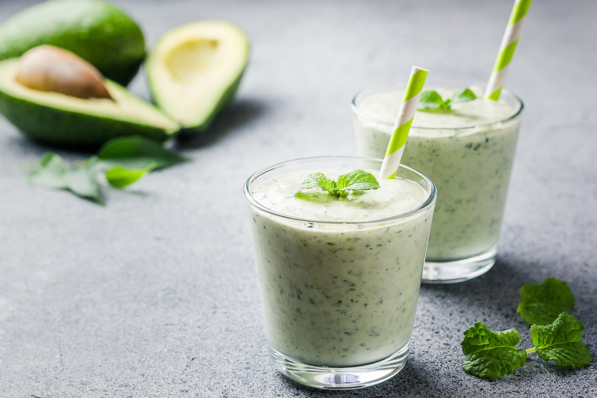 Two green smoothies with green straws, made with avocado, mint, spinach, banana, and chia seeds.