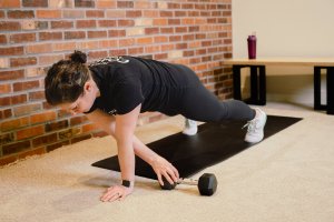 Coach Heather performs reps of plank pull throughs on a yoga mat on the floor during a core workout.