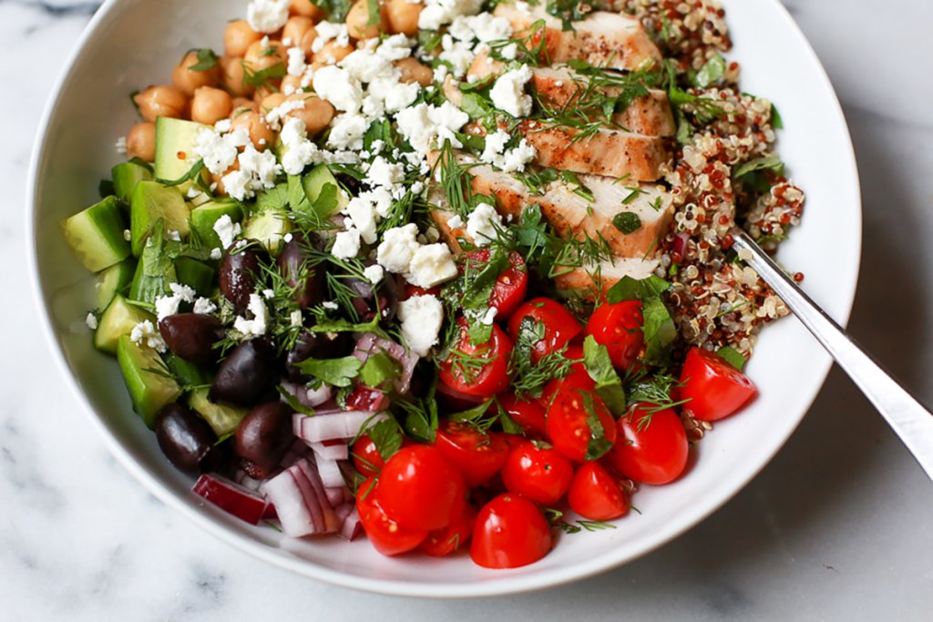 Greek bowl with tomatoes, feta, quinoa, chickpeas, cucumber, olives, red onion and herbs.