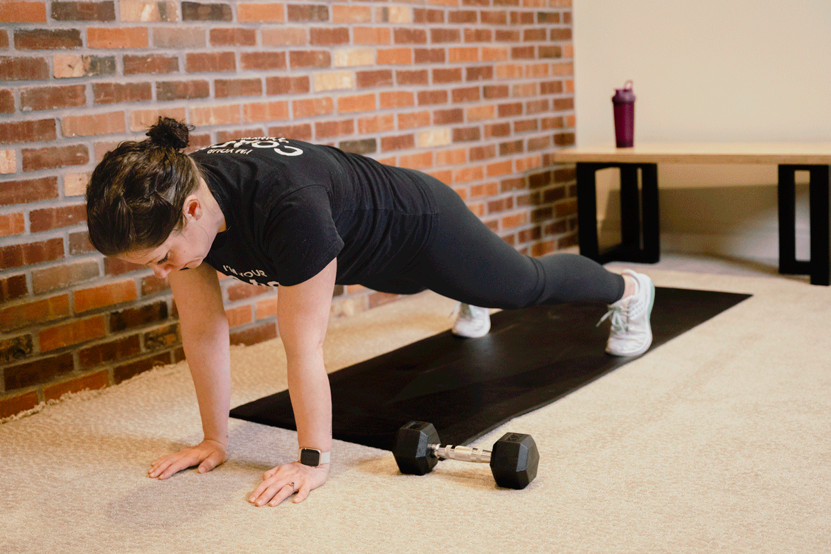 Coach Heather performs reps of plank pull throughs on a yoga mat on the floor.