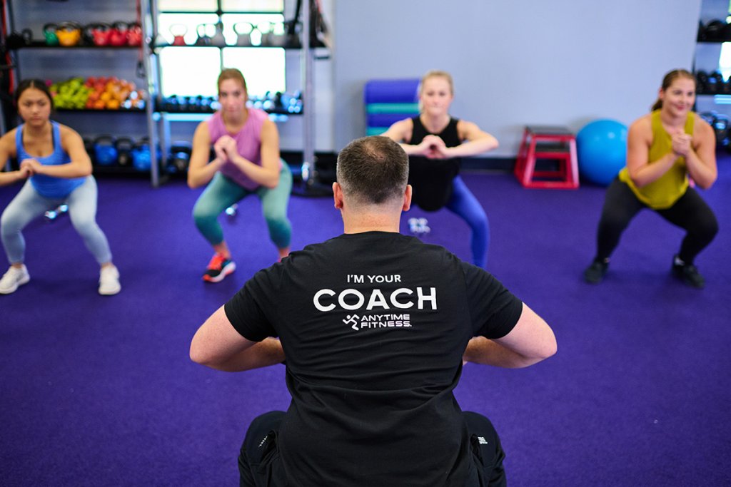 A fitness coach leads a group fitness class with four women.