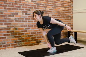 Coach Heather demonstrating a single-leg squat reach for leg workouts at home.