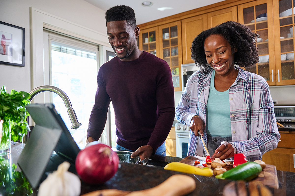Happy couple preparing a healthy meal together in a modern kitchen with fresh vegetables on the counter.
