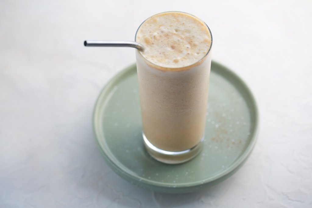 Blended protein shake in a glass with a creamy layer of foam on top and a straw ready for drinking.