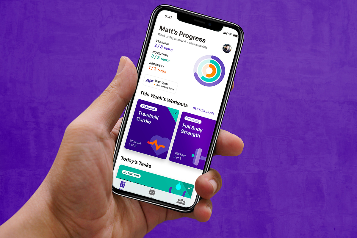 A person holds a phone displaying a personalized workout plan, including cardio and strength workouts, in the Anytime Fitness App.