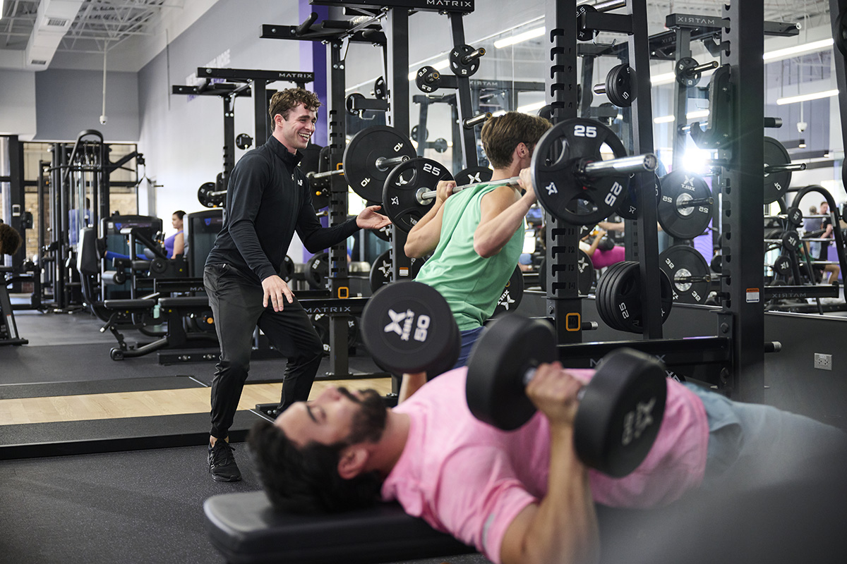 An Anytime Fitness Coach leads a training session for a group performing squats with resistance bands.