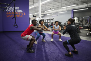 An Anytime Fitness Coach leads a training session for a group performing squats with resistance bands.