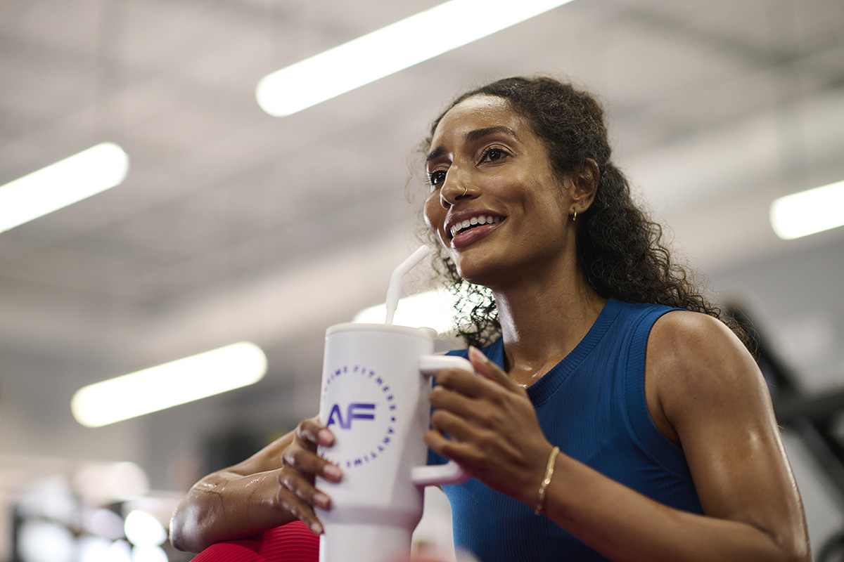 Woman in a gym setting taking a sip from an Anytime Fitness water bottle during a rest period.