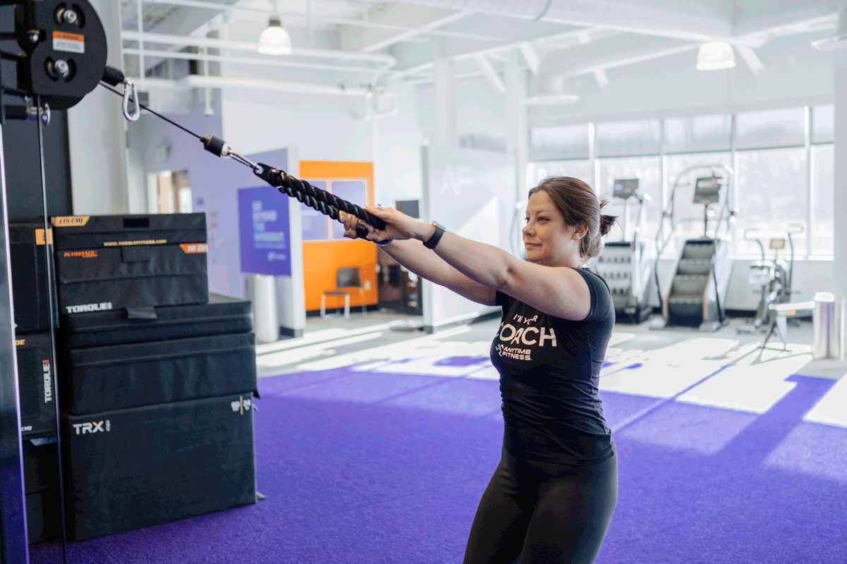 An Anytime Fitness Coach demonstrating a cable face pull, targeting the rear deltoid muscles.