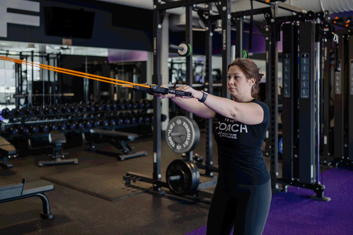 An Anytime Fitness Coach demonstrating a high row exercise with a resistance band.