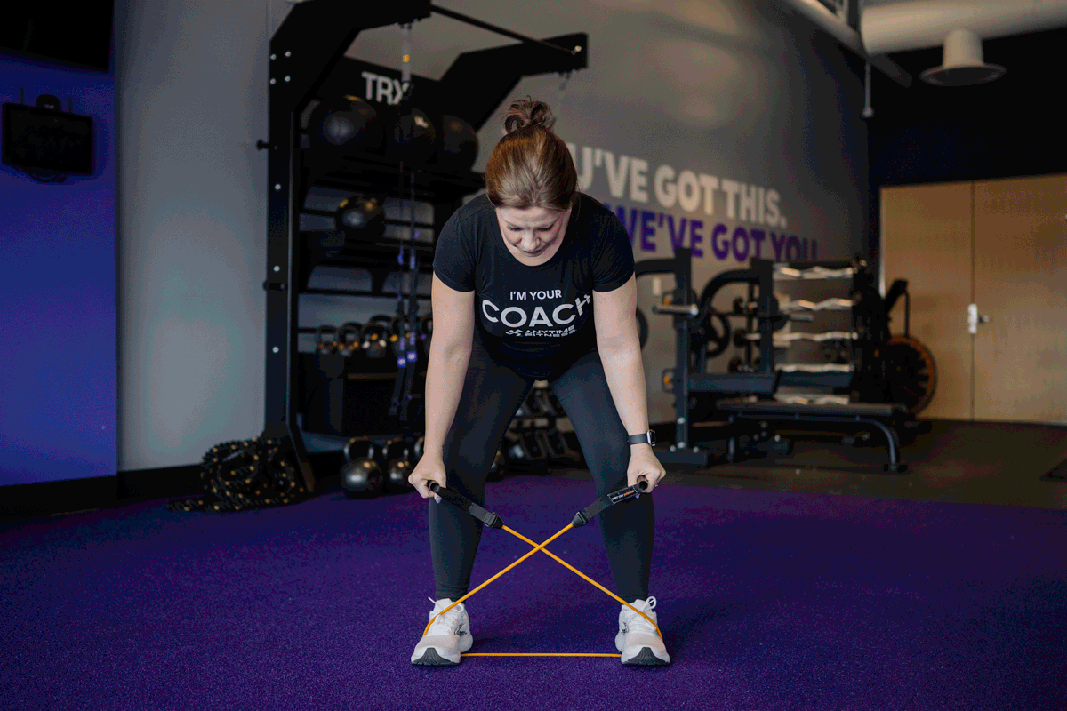 An Anytime Fitness Coach using a resistance band to perform a reverse fly exercise.